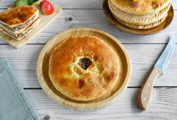 The traditional dish of the peoples of the Caucasus is Karachai khychins (Ossetian pies) with meat on a wooden board. Light wooden background, top view, copy space.