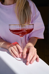 A glass of red wine, champagne or a cocktail in the hands of a girl relaxing in a restaurant. Tasting of alcoholic beverages. Summer rest. Romantic evening aperitif. Close-up of a glass of wine
