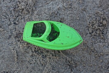 one dirty green plastic small boat toy stands on gray sand in a sandbox outside