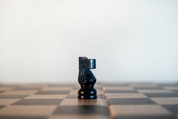 Black chess knight piece on the board on a white background. © Wacha Studio
