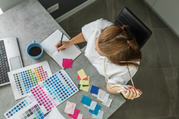 Fototapeta na wymiar Woman sits at table in modern office next to color palette and fabric samples for design project.