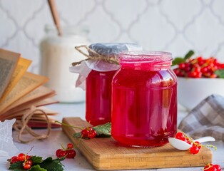Redcurrant jam in a glass jar on a wooden board on a light concrete background. Preparations, conservation of the harvest.