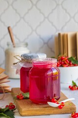 Redcurrant jam in a glass jar on a wooden board on a light concrete background. Preparations, conservation of the harvest.