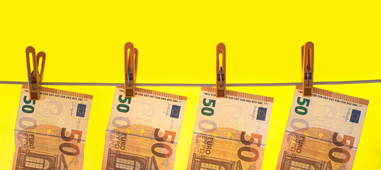 Part of fifty-net Euro banknotes pinned to a rope on a yellow background. widescreen photo