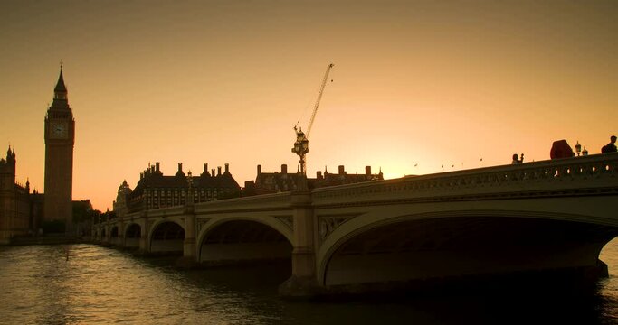 Anonymous eople and traffic crossing Westminster Bridge at sunset by Big Ben and the Houses of Parliament, London, England
