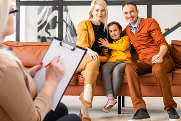 Rear view of female psychologist helping young family with a kid to solve child development problems. Family sitting on a sofa