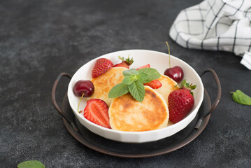 Cottage cheesecakes with berries and mint in a white plate on a dark background.