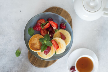 Cottage cheesecakes with berries and mint in a grey plate on a grey background.
