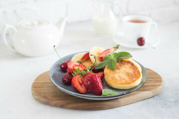 Cottage cheesecakes with berries and mint in a grey plate on a white background teapot and cup of tea.