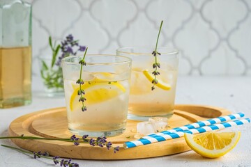 Lemonade with lavender syrup, lemon slices and ice on a wooden board on a light concrete background. Recipes for non-alcoholic refreshing drinks. Summer concept