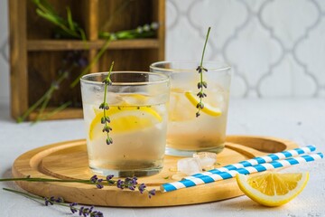 Lemonade with lavender syrup, lemon slices and ice on a wooden board on a light concrete background. Recipes for non-alcoholic refreshing drinks. Summer concept