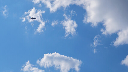 The passenger airplane is flying far away in the blue sky and white clouds. Aircraft in the air. Light background or backdrop about international passenger air transportation