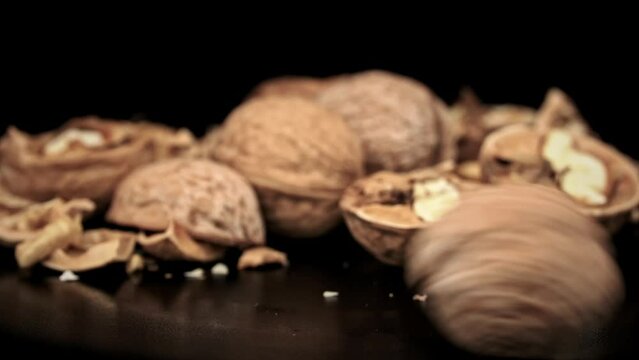 Whole walnut rolls in slow motion against a background of pile of nuts in a loop. A lot of walnuts in the shell rotate on a black background. Nuts are good for the brain. Heap of walnuts close-up.