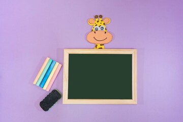 Funny background with school material, on purple background. Blackboard, chalk, eraser and eva rubber giraffe made by a child. Space for text.