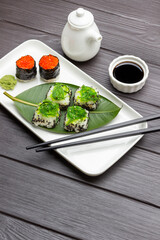 Seaweed sushi on green leaf, caviar sushi and chopsticks on plate.