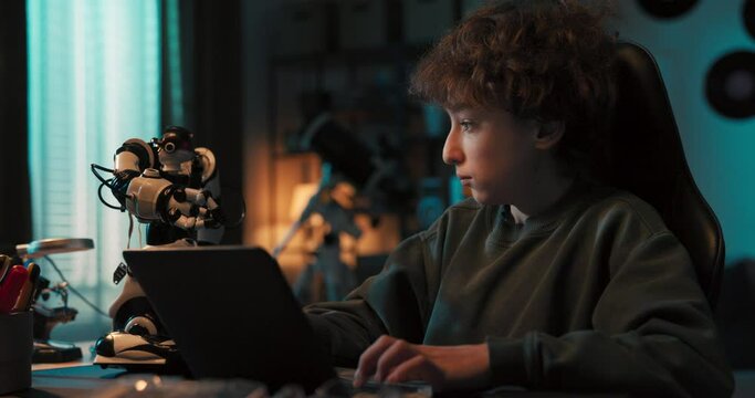 Teenager sits in room in the dark and programs a robot on laptop, adds new features, high-fives it, interest in robotics technology.