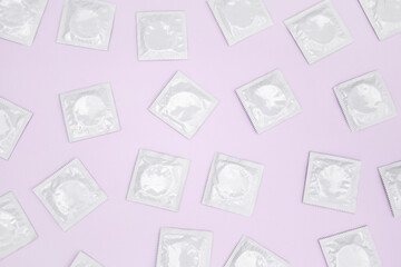 Many white packages of unopened condoms on a pink background.