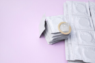 Many white packages of unopened condoms on a pink background.