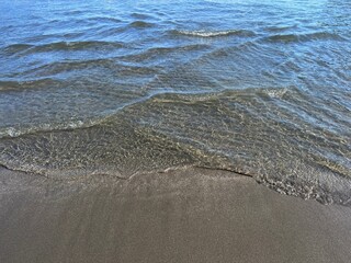 Sea waves on the beach with volcanic sand. Clear shiny sea water.