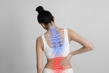 Woman suffering from pain in back on light background