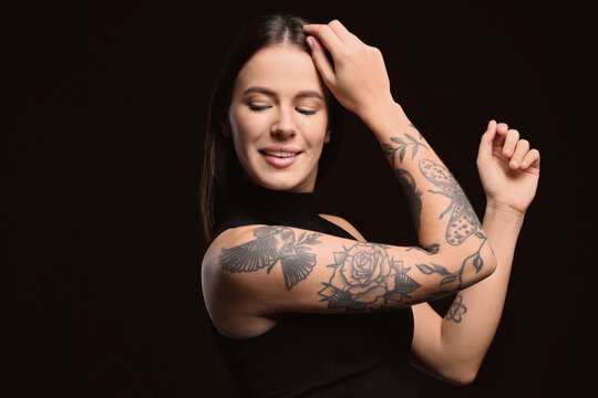 Beautiful woman with tattoos on arms against black background. Space for text
