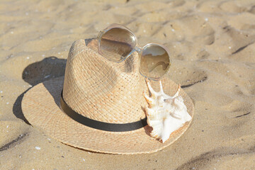 Fototapeta na wymiar Stylish straw hat, sunglasses and sea shell on sandy beach