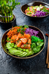 Poke with salmon, avocado, chukka, cabbage and carrot on black plate on dark stone table vertical