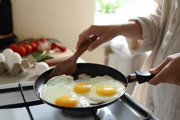 Woman cooking tasty eggs on frying pan in kitchen, closeup