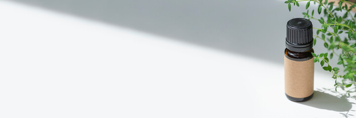 Amber bottle with craft label thyme essential oil. White background with daylight and beautiful shadows. Skincare products, natural cosmetic. Beauty concept for face and body care