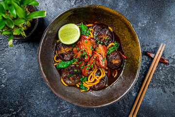 chicken wok noodles with mushrooms, vegetables and lime on dark stone table top view