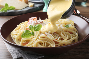 Pouring tasty cheese sauce onto spaghetti with meat on wooden table, closeup