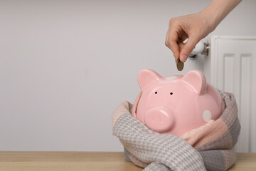 Woman putting coin into piggy bank near heating radiator, closeup. Space for text