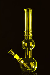 Glass bong on black background, toned in yellow. Smoking device