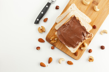 Square bread for toast with chocolate paste on a wooden board. Nuts, a knife and a wooden cutting...