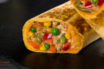 Mexican chicken burrito with spices, vegetables and cheese on black stone plate macro close up
