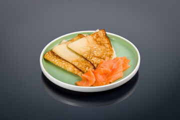 pancakes with smoked salmon on green plate on black with reflection