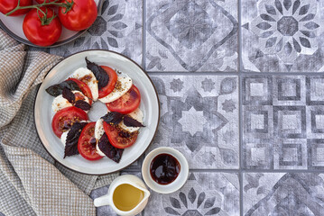 Caprese salad with mozzarella, red tomatoes and purple basil, dressed with olive oil, Dijon mustard and balsamic. Ceramic plate with caprese salad on a gray kitchen table. Top view. Copy space.