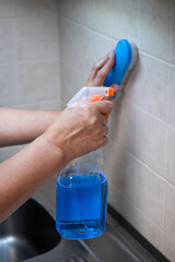 A man's hand cleans a tile wall with a blue brush