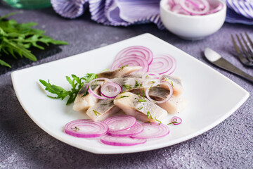 Sliced salted herring with onions and arugula on a plate on the table. Simple snack