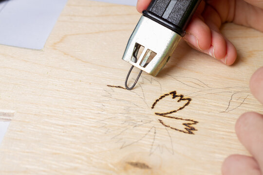 Burn out a drawing on a wooden board with an electric device with a scorcher