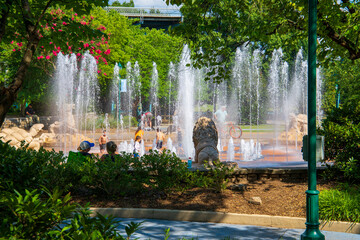 children playing in a water fountain surrounded by a gorgeous summer landscape with pink trees and...