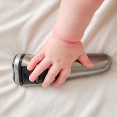 The hand of a baby toddler boy is holding an electric razor. Child with a silver safety razor, close-up