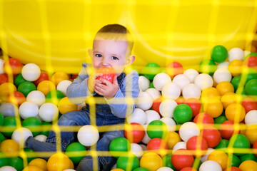Fototapeta na wymiar Happy toddler baby boy plays with plastic balls in the playroom. Kid age one year