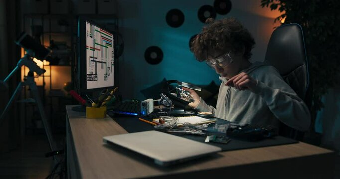 The little engineer sits at desk wearing safety goggles and developing his passion for soldering. The child learns to use equipment to repair electronics, solders cables, wires.