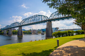 the Walnut Street Bridge over the rippling blue waters of the Tennessee river with rocks along the...
