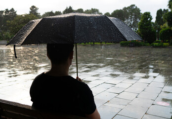 Batumi, Georgia - July 10, 2022: a man sits under an umbrella on a bench in the rain