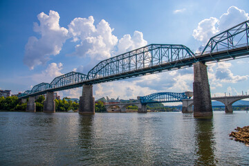 the Walnut Street Bridge over the rippling blue waters of the Tennessee river with rocks along the...