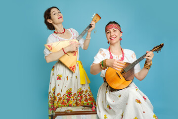 Women musicians in Russian folk dresses with musical instruments on a blue studio background. Happy...