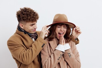a cute couple stands on a white background in autumn clothes and the guy adjusts the hat on the woman's head looking at her with love, and the woman smiles happily