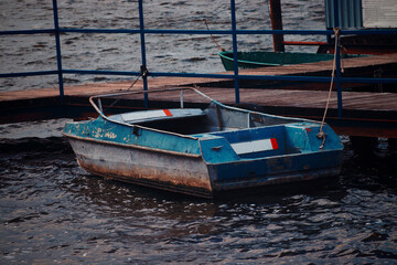 Fototapeta na wymiar Rusty blue river boat moored to the pier. Cold windy weather and dark blue lake water. Abandoned place concept